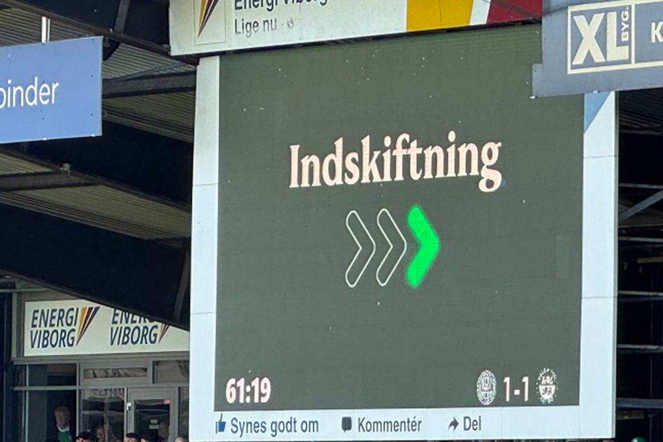 En fodboldstadionresultattavle viser "Indskiftning" med grønne pile og stillingen 1-1.